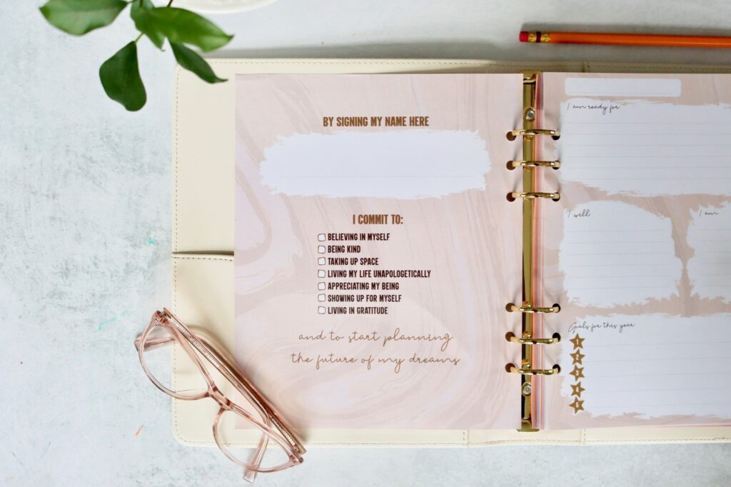 Self Funding Planner is open to one of the front pages asking the user to sign their name to commit to being kind, living in gratitude, and more. There is a pair of glasses laying on top of the planner.