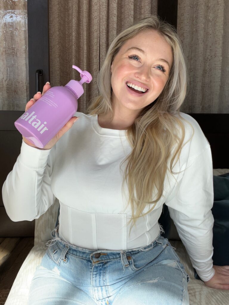 Iskra holding an Island Orchid Saltair body wash in one hand and smiling.